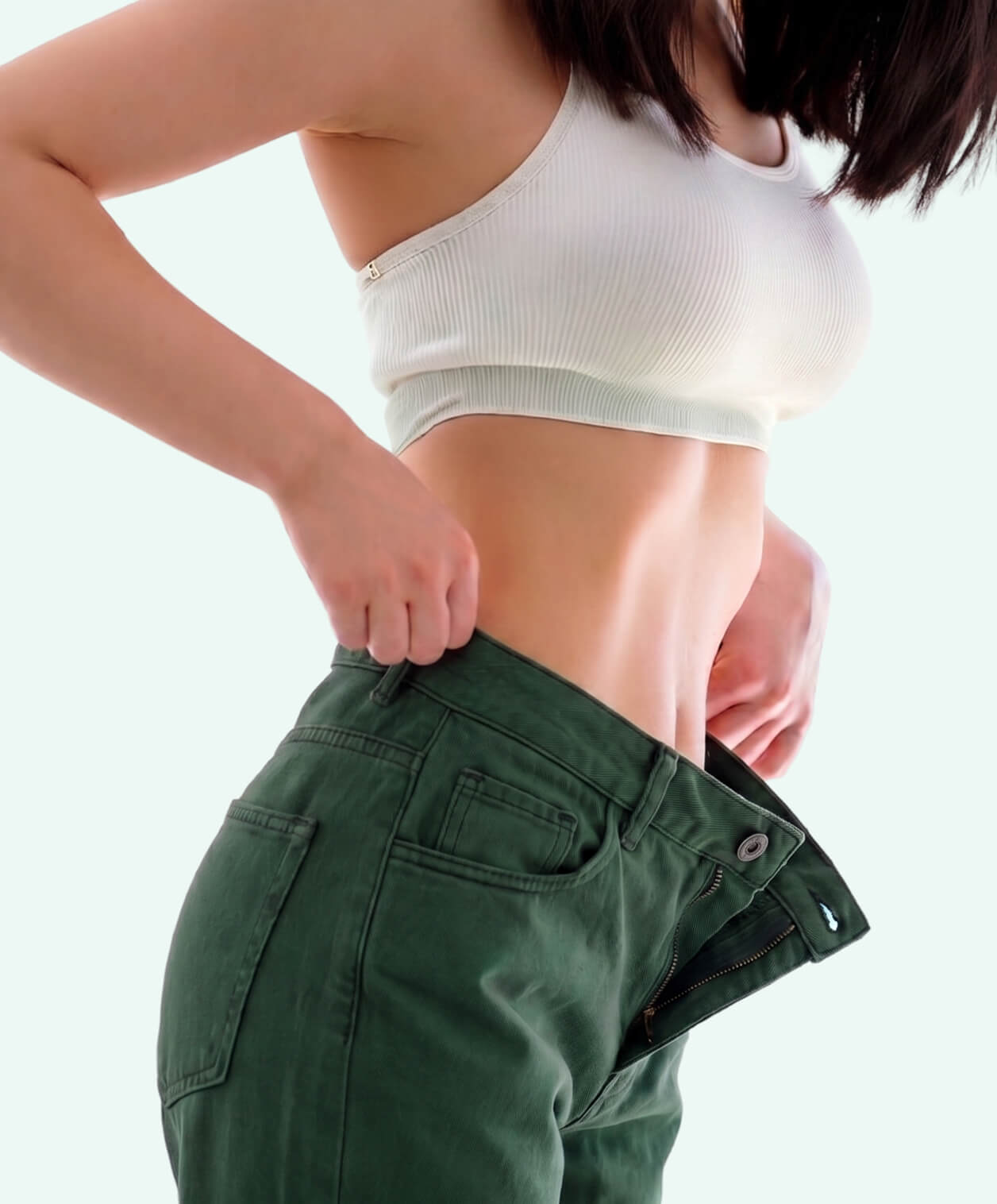 Woman pulling away the loose waistband of her green jeans, demonstrating a flat stomach and no bloating after passing the zipper test.